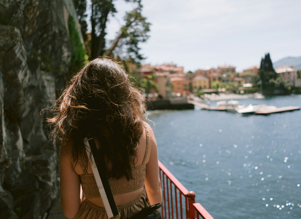 showing the back of a woman walking on a sidewalk, with the sea to her right